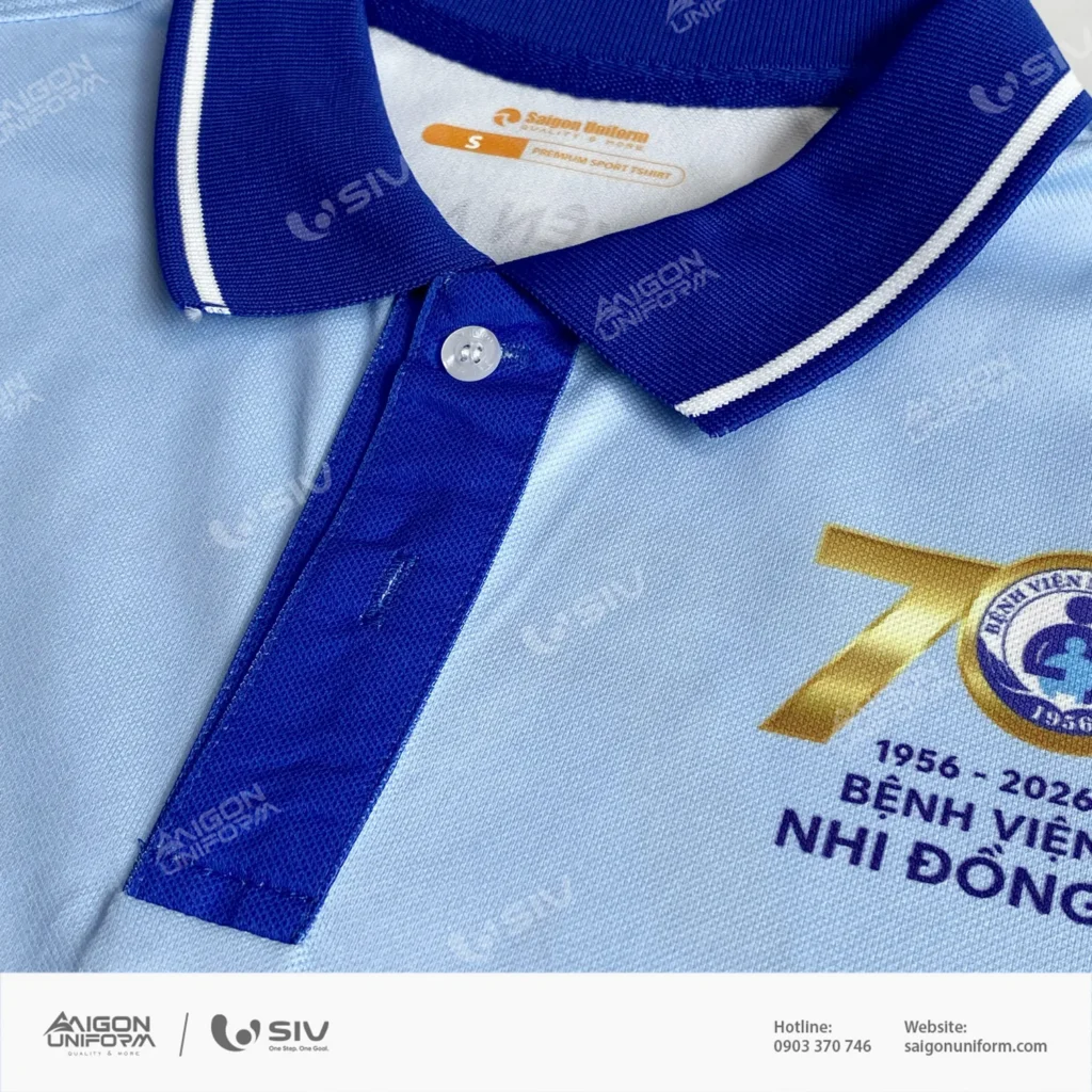 Bo cổ dệt liền hai sọc trắng, nẹp khuy phối xanh đậm và nhãn dệt Saigon Uniform Premium Sport Tshirt bên trong cổ áo. Cận cảnh bo cổ dệt hai sọc trắng và nhãn dệt Saigon Uniform size S trên áo polo đồng phục Bệnh viện Nhi Đồng 1